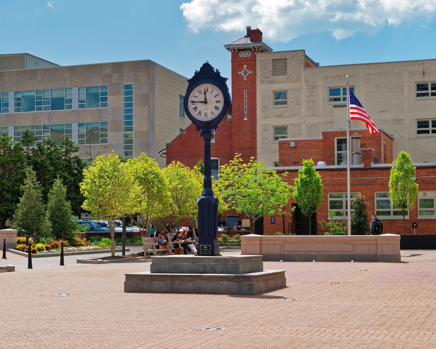 University campus plaza with a clock post, flagpole, and brick and stone academic buildings