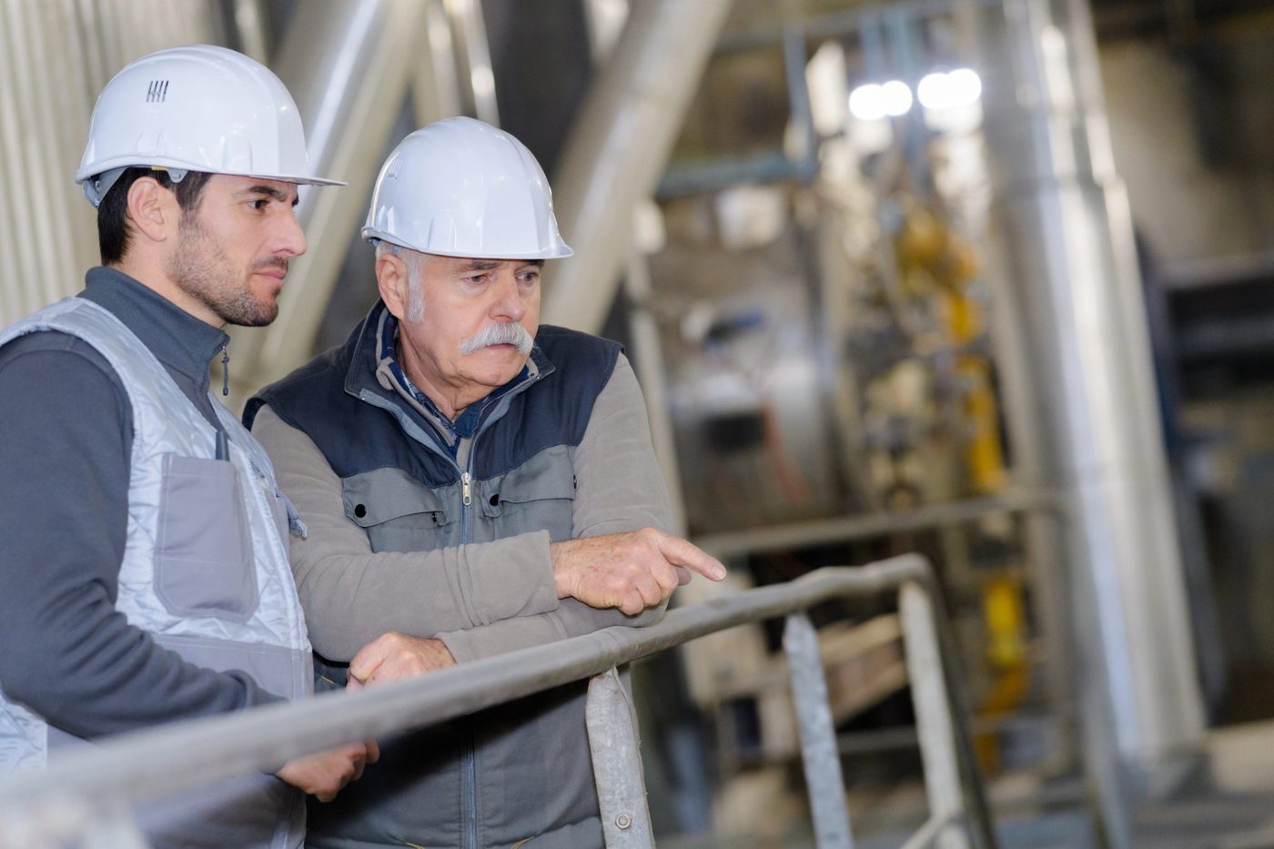 Two facilities staff in hard hats reviewing equipment in a mechanical space